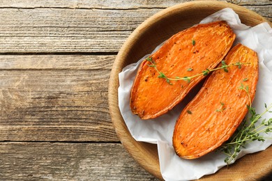 Photo of Halves of tasty cooked sweet potato with thyme on wooden table, top view. Space for text