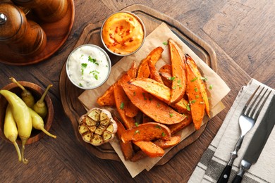 Photo of Tasty cooked sweet potatoes served with sauces on wooden table, top view