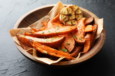 Photo of Tasty cooked sweet potatoes with parsley and garlic on black table, closeup