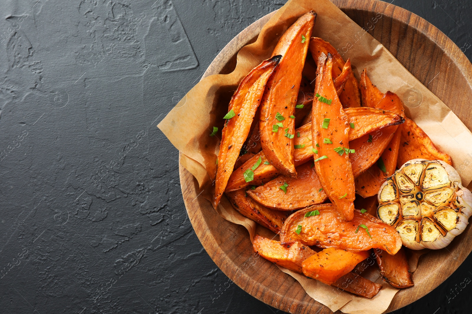 Photo of Tasty cooked sweet potatoes with garlic on black table, top view. Space for text