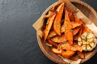 Tasty cooked sweet potatoes with garlic on black table, top view. Space for text