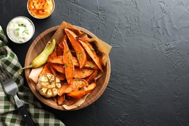 Photo of Tasty cooked sweet potatoes with garlic, pickled pepper and sauces on black table, top view. Space for text