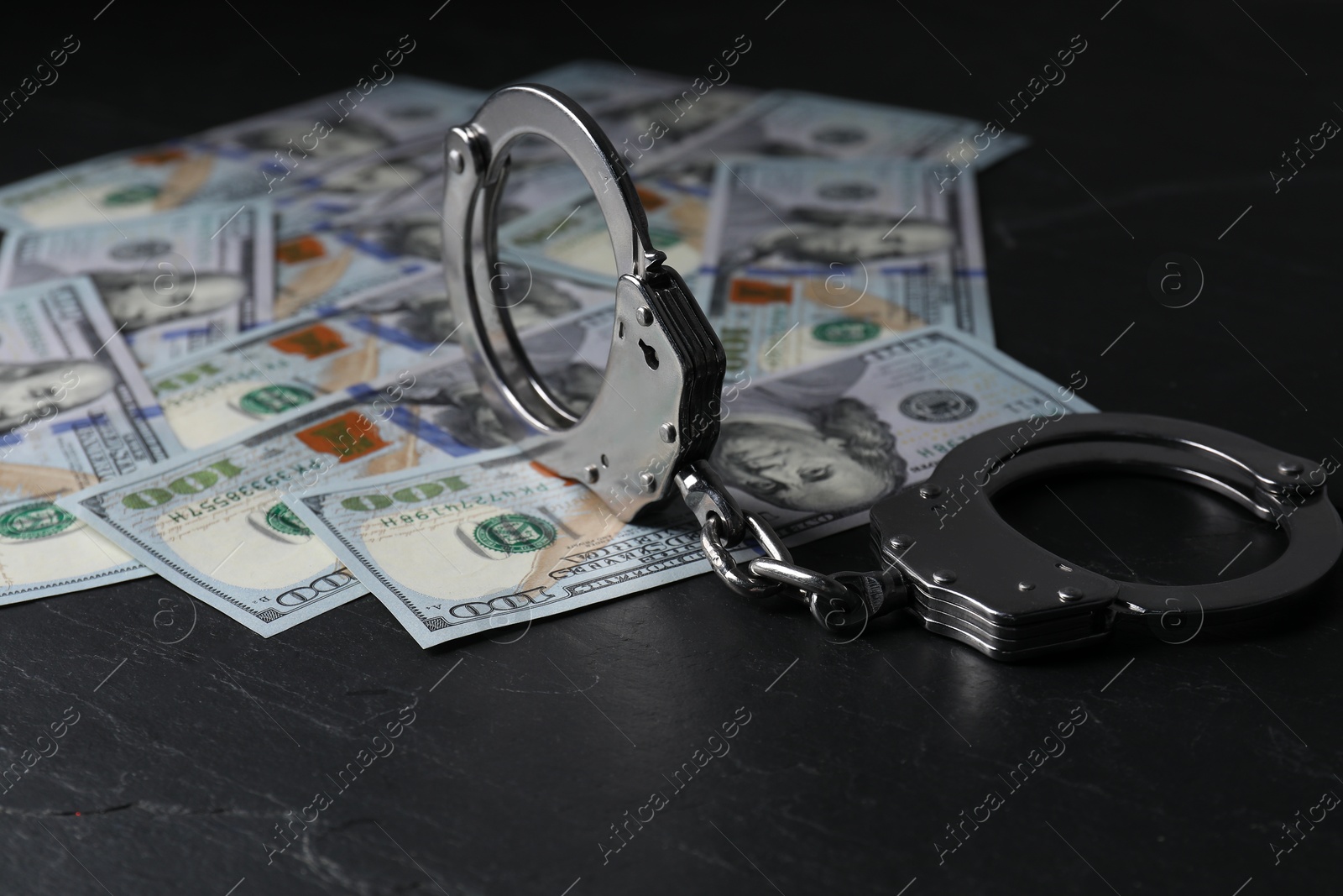 Photo of Corruption. Handcuffs and dollar banknotes on black table, closeup