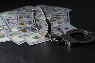 Photo of Corruption. Handcuffs and dollar banknotes on black table, closeup