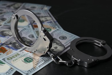 Photo of Corruption. Handcuffs and dollar banknotes on black table, closeup