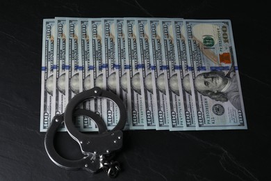 Photo of Corruption. Handcuffs and dollar banknotes on black table, above view