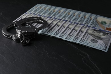 Photo of Corruption. Handcuffs and dollar banknotes on black table