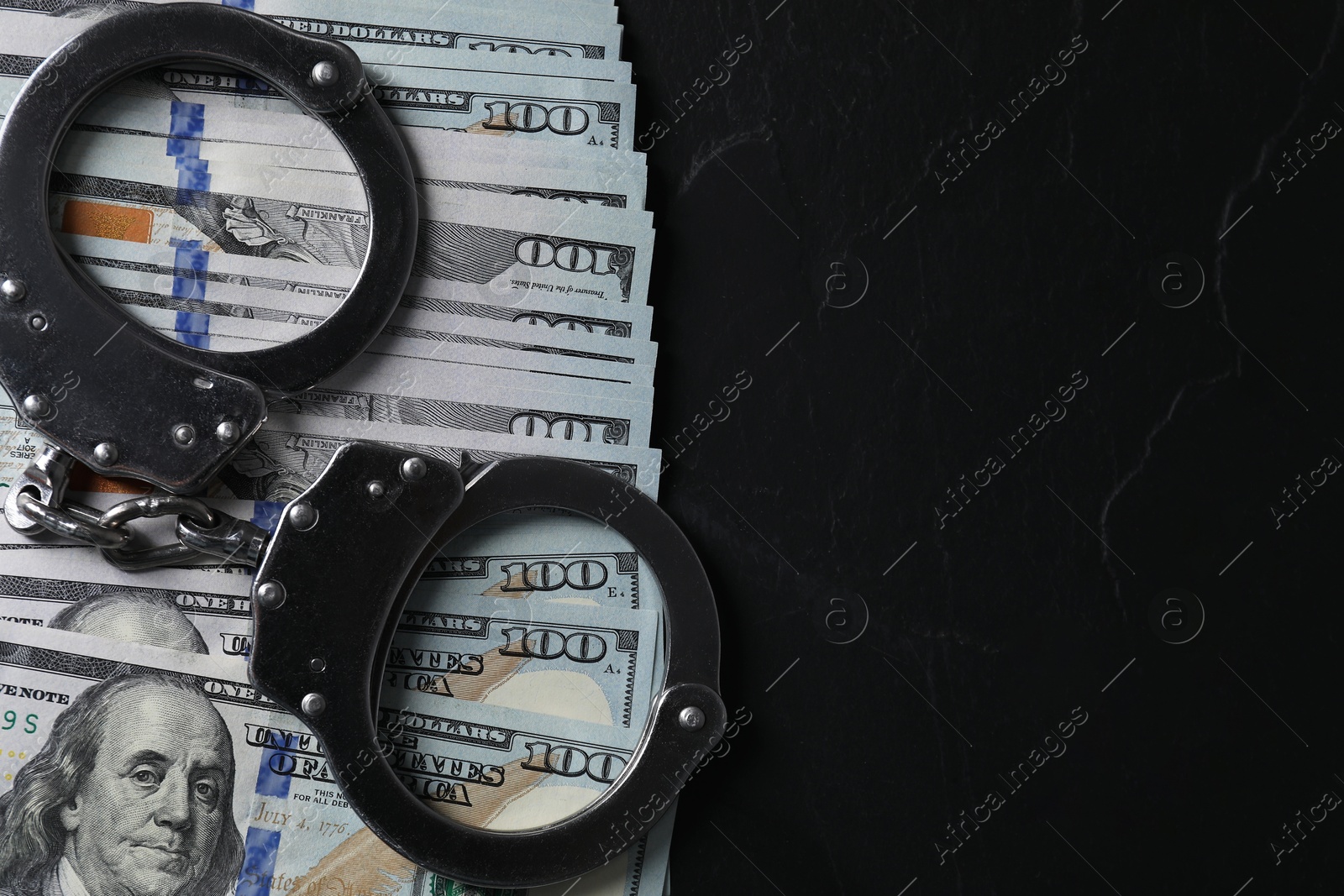 Photo of Corruption. Handcuffs and dollar banknotes on black table, top view. Space for text