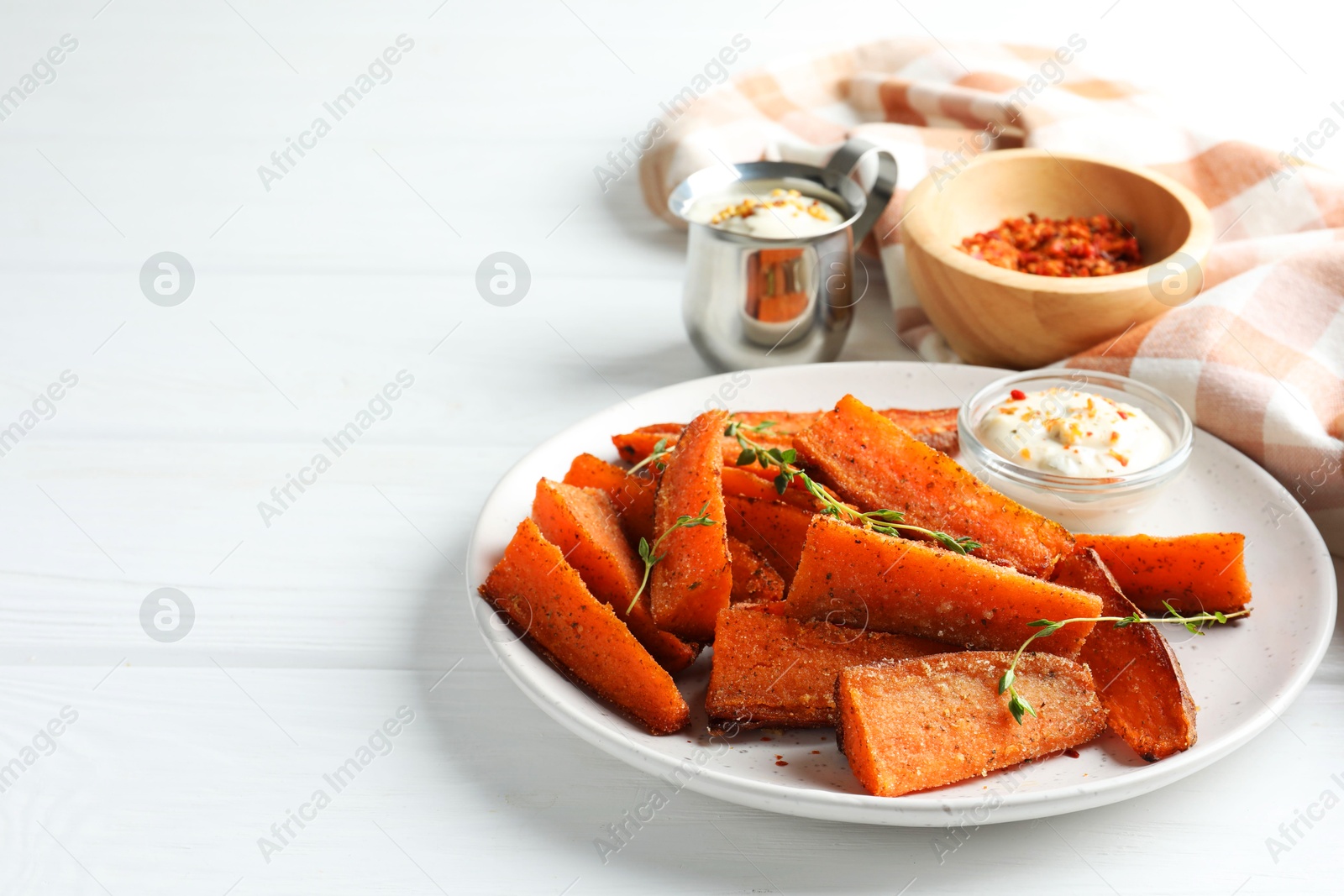 Photo of Pieces of tasty baked sweet potato with microgreens served on white wooden table, space for text