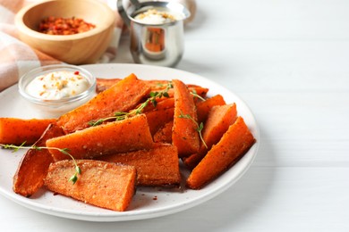 Pieces of tasty baked sweet potato with microgreens served on white wooden table, closeup