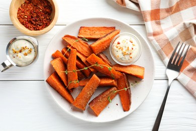 Pieces of tasty baked sweet potato with microgreens served on white wooden table, flat lay