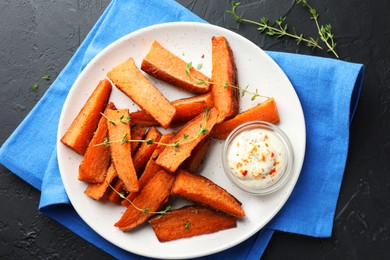 Photo of Pieces of tasty baked sweet potato with microgreens and sauce on grey textured table, flat lay