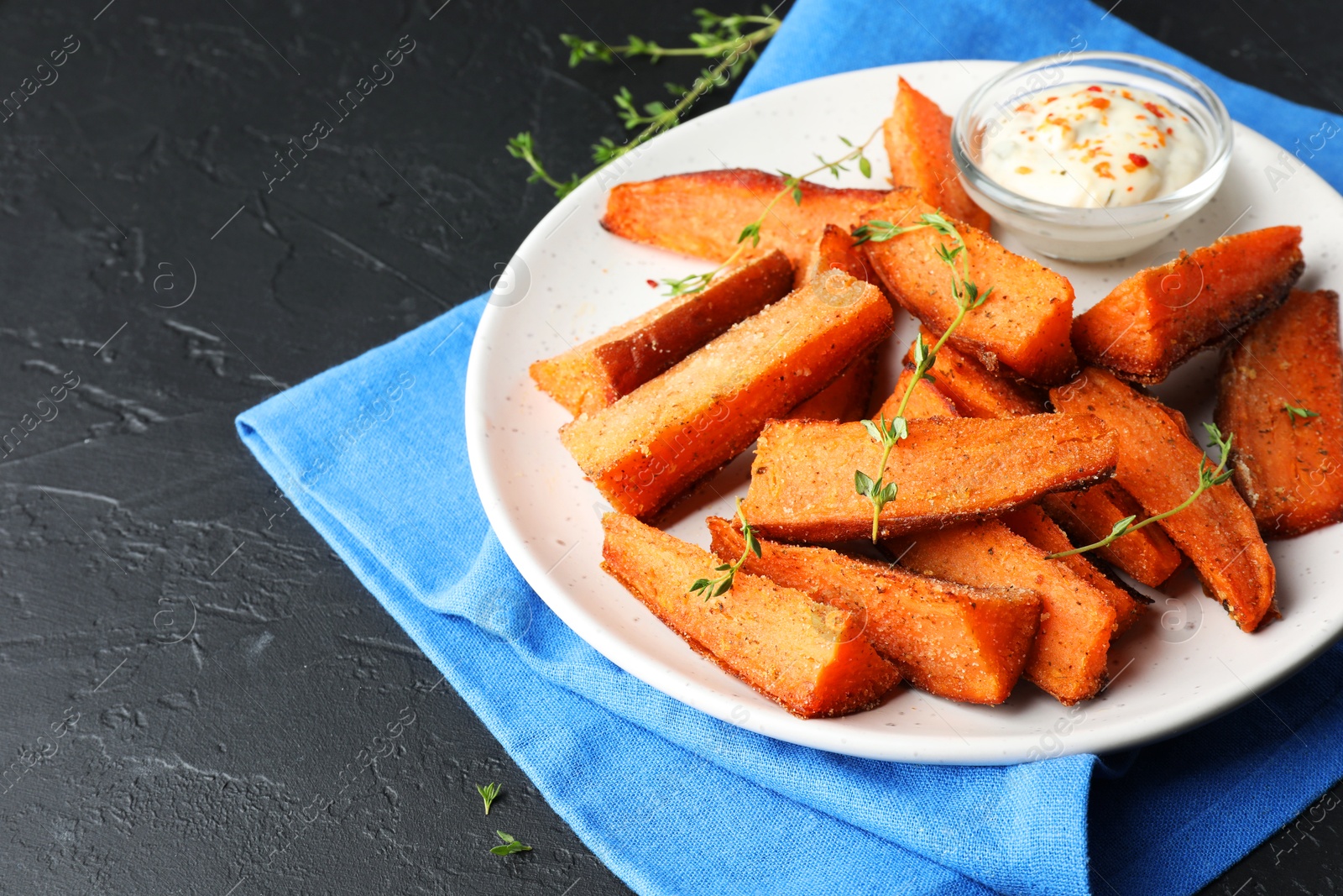 Photo of Pieces of tasty baked sweet potato with microgreens and sauce on grey textured table, closeup