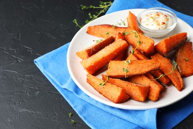 Pieces of tasty baked sweet potato with microgreens and sauce on grey textured table, closeup