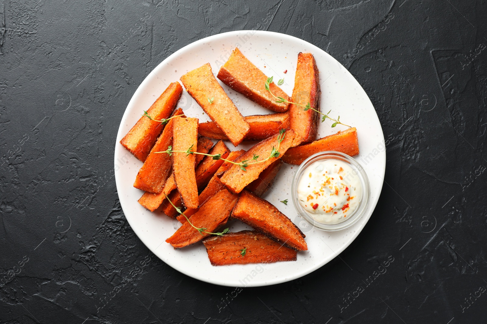 Photo of Pieces of tasty baked sweet potato with microgreens and sauce on grey textured table, top view