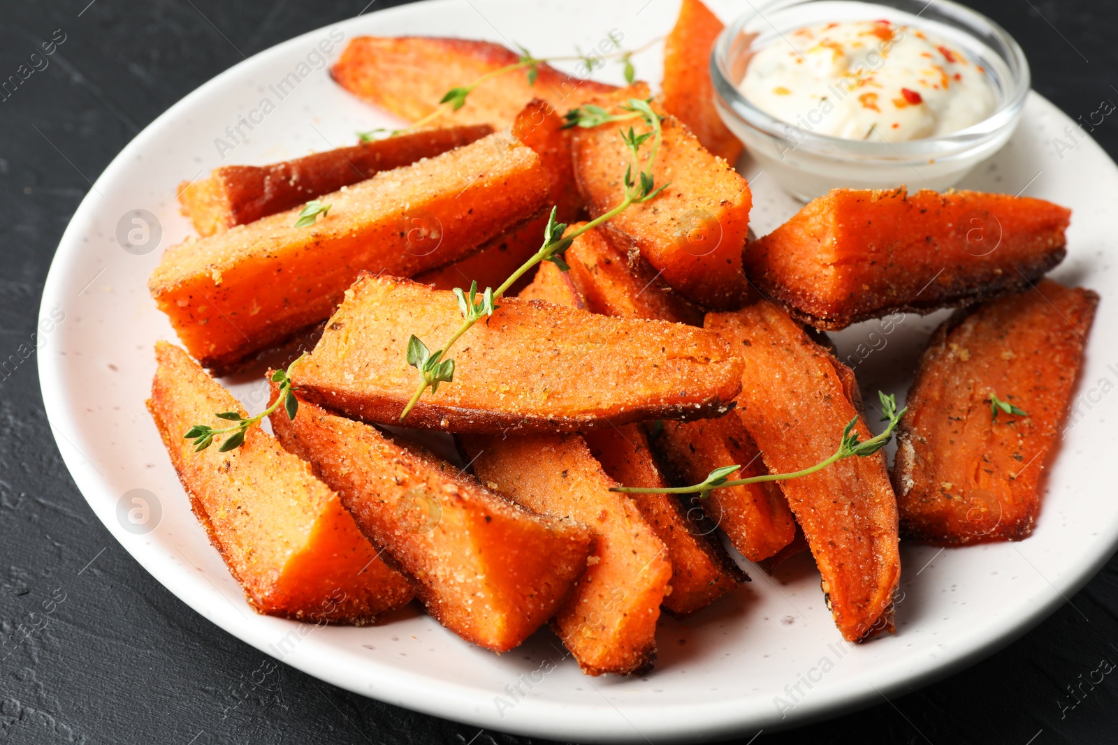 Photo of Pieces of tasty baked sweet potato with microgreens and sauce on grey table, closeup