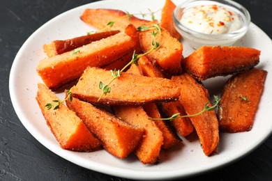 Photo of Pieces of tasty baked sweet potato with microgreens and sauce on grey table, closeup