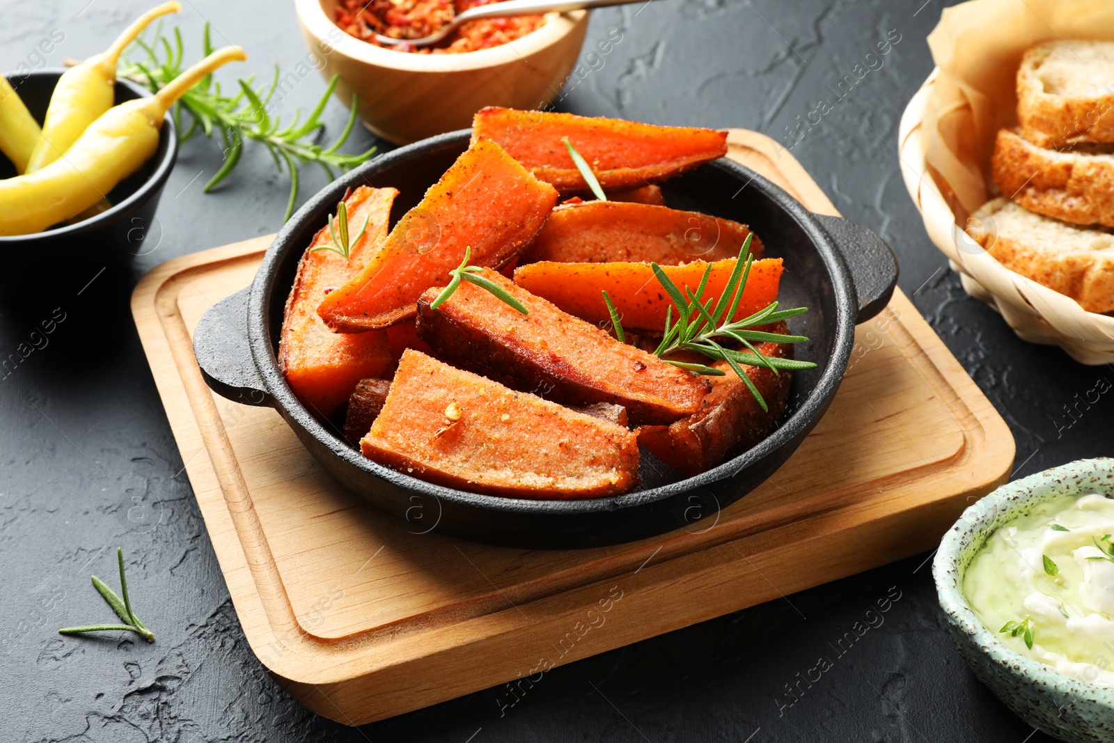 Photo of Pieces of tasty cooked sweet potato with rosemary in baking dish served on grey textured table