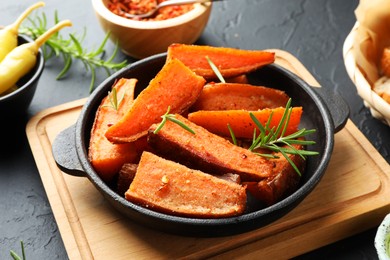 Pieces of tasty cooked sweet potato with rosemary in baking dish served on grey textured table, closeup