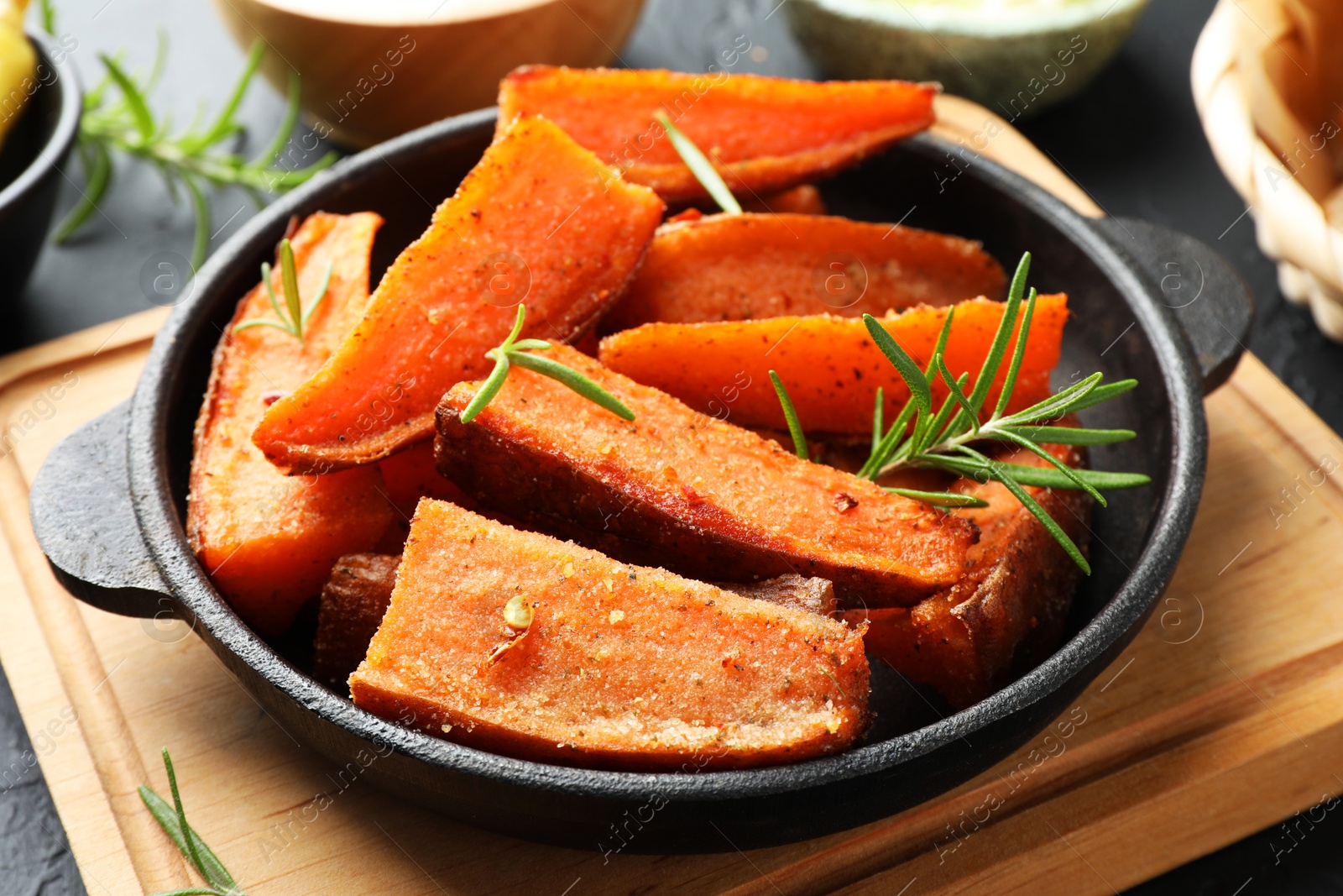 Photo of Pieces of tasty cooked sweet potato with rosemary in baking dish served on grey table, closeup