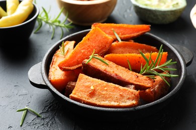 Pieces of tasty cooked sweet potato with rosemary in baking dish served on grey textured table, closeup