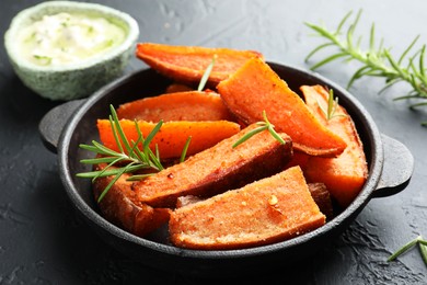 Photo of Pieces of tasty cooked sweet potato with rosemary in baking dish served on grey textured table, closeup