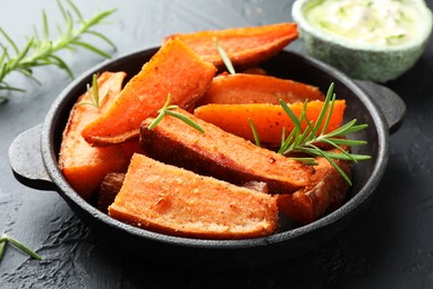 Photo of Pieces of tasty cooked sweet potato with rosemary in baking dish served on grey textured table, closeup