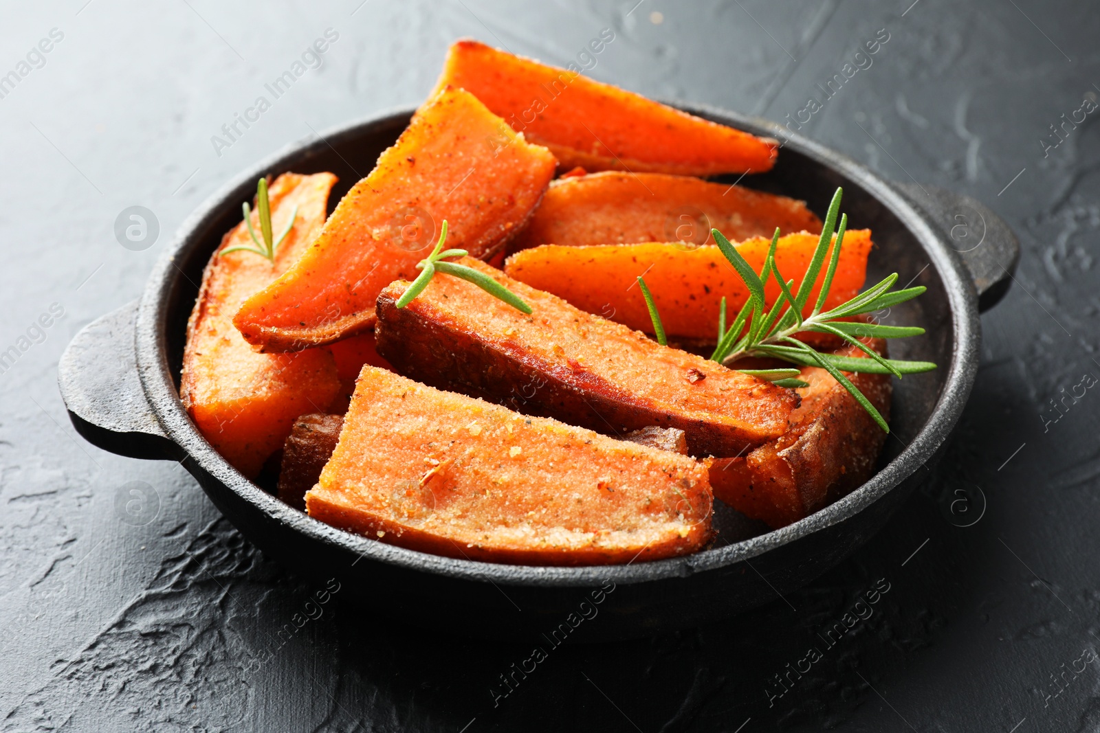 Photo of Pieces of tasty cooked sweet potato with rosemary in baking dish on grey textured table, closeup