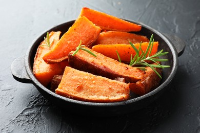 Pieces of tasty cooked sweet potato with rosemary in baking dish on grey textured table, closeup