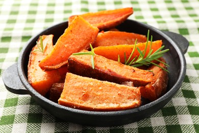 Pieces of tasty cooked sweet potato with rosemary in baking dish on checkered tablecloth, closeup