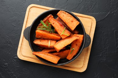 Pieces of tasty cooked sweet potato with rosemary in baking dish on grey textured table, top view