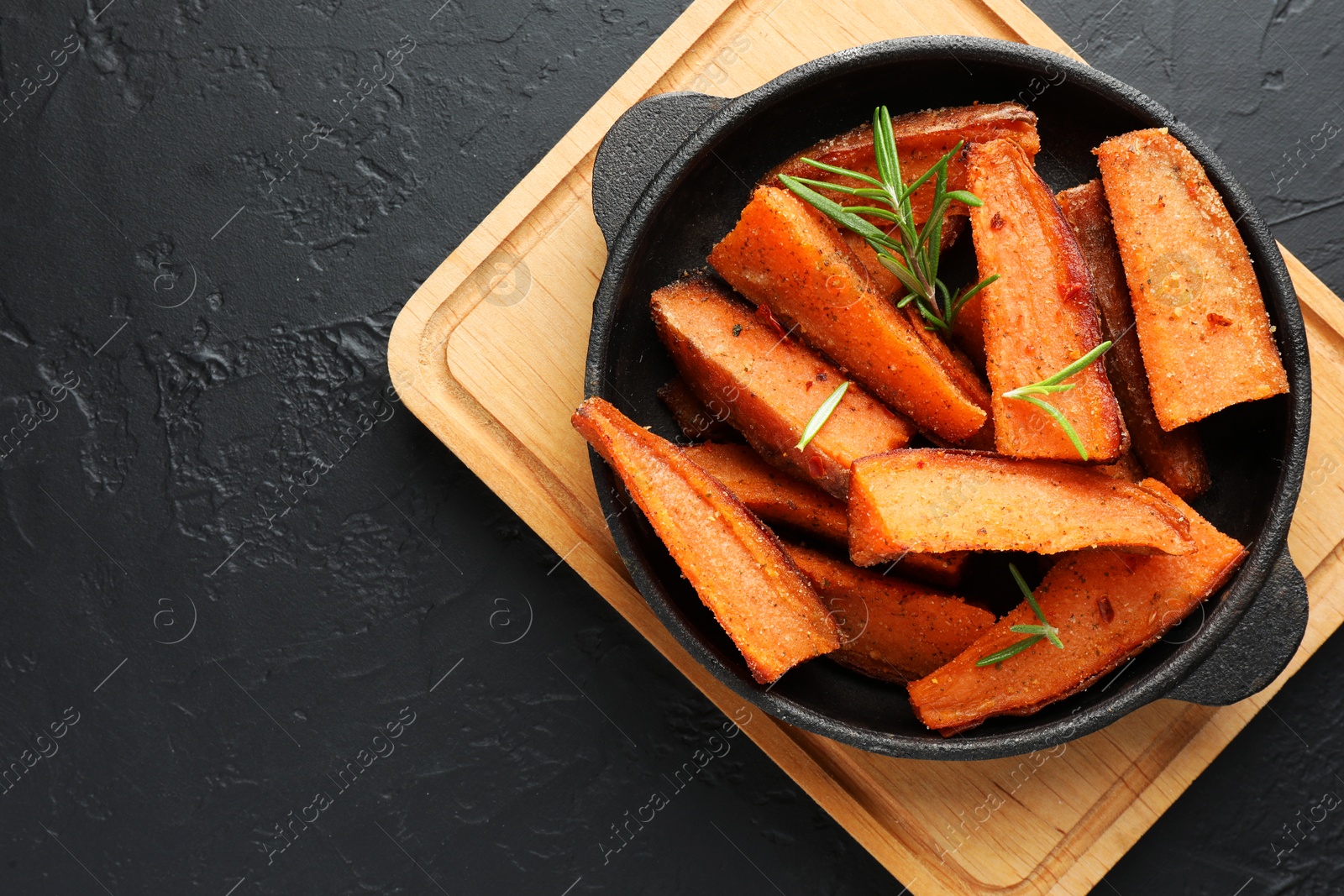 Photo of Pieces of tasty cooked sweet potato with rosemary in baking dish on grey textured table, top view. Space for text