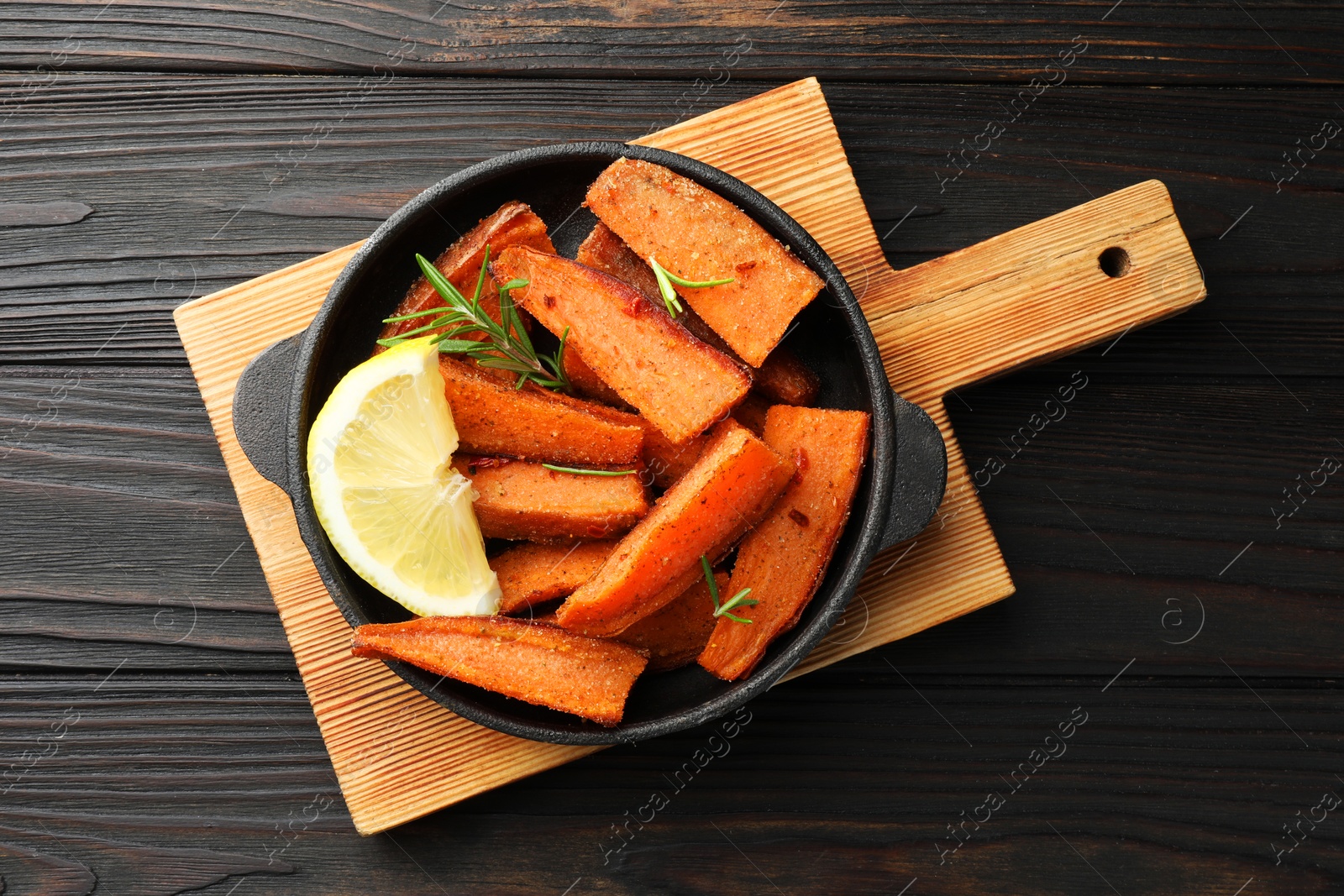 Photo of Pieces of tasty cooked sweet potato with rosemary and lemon in baking dish on wooden table, top view