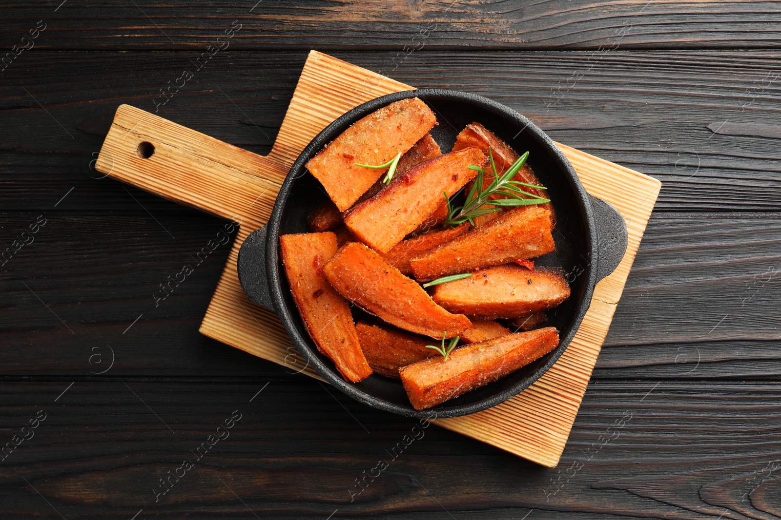 Photo of Pieces of tasty cooked sweet potato with rosemary in baking dish on wooden table, top view