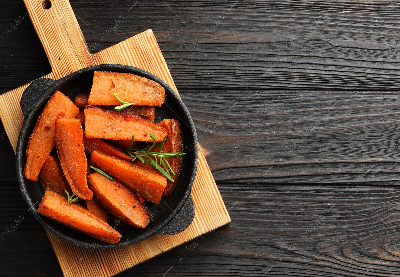 Photo of Pieces of tasty cooked sweet potato with rosemary in baking dish on wooden table, top view. Space for text