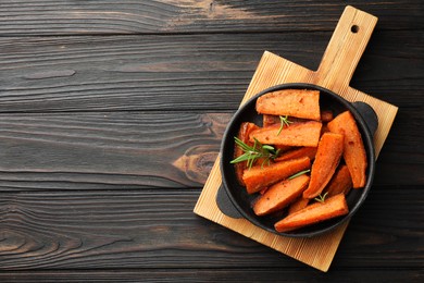 Photo of Pieces of tasty cooked sweet potato with rosemary in baking dish on wooden table, top view. Space for text