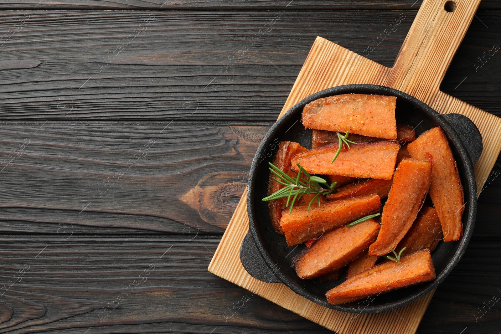 Photo of Pieces of tasty cooked sweet potato with rosemary in baking dish on wooden table, top view. Space for text