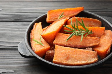 Photo of Pieces of tasty cooked sweet potato with rosemary in baking dish on wooden table, closeup