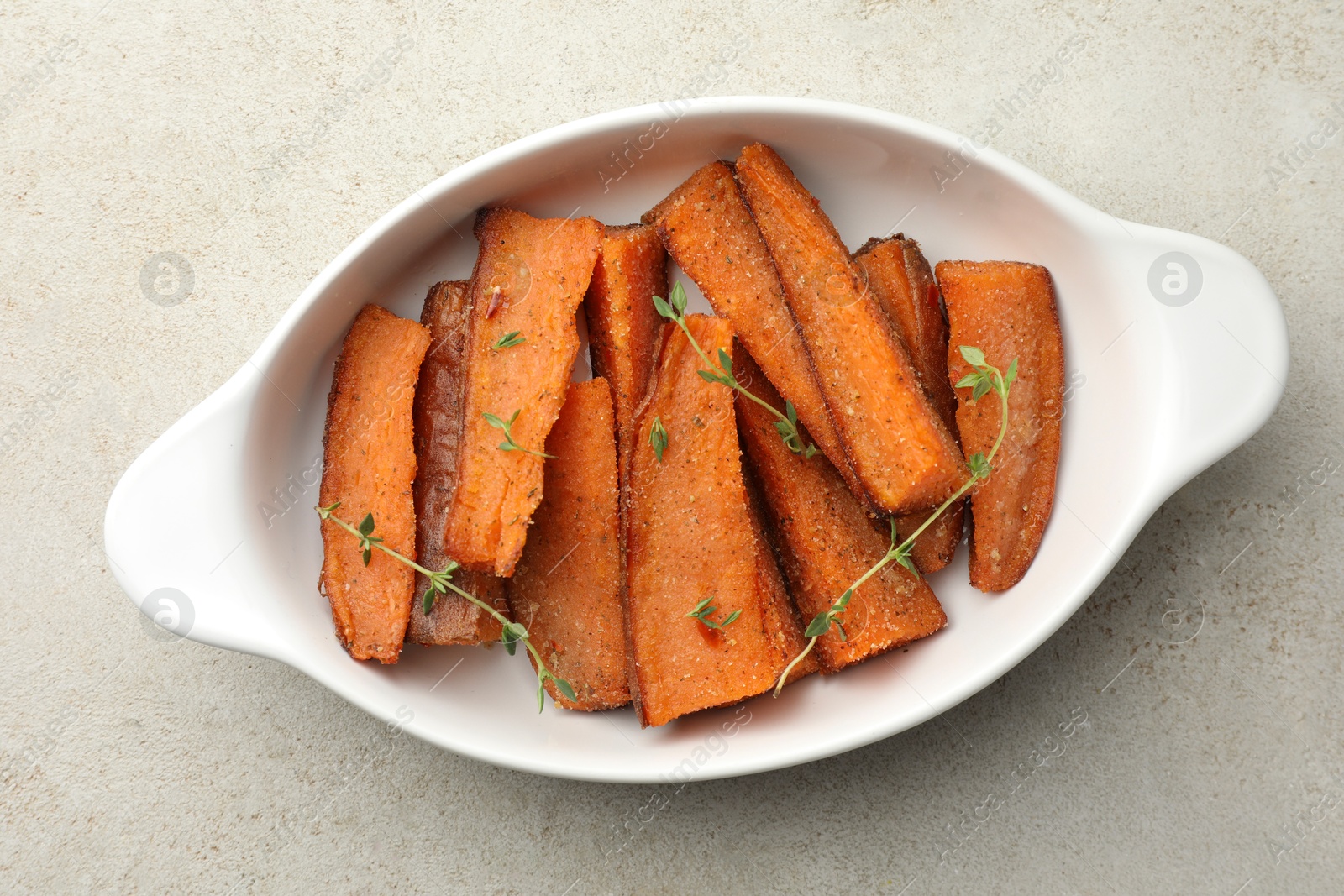 Photo of Pieces of tasty cooked sweet potato with microgreens in baking dish on light textured table, top view