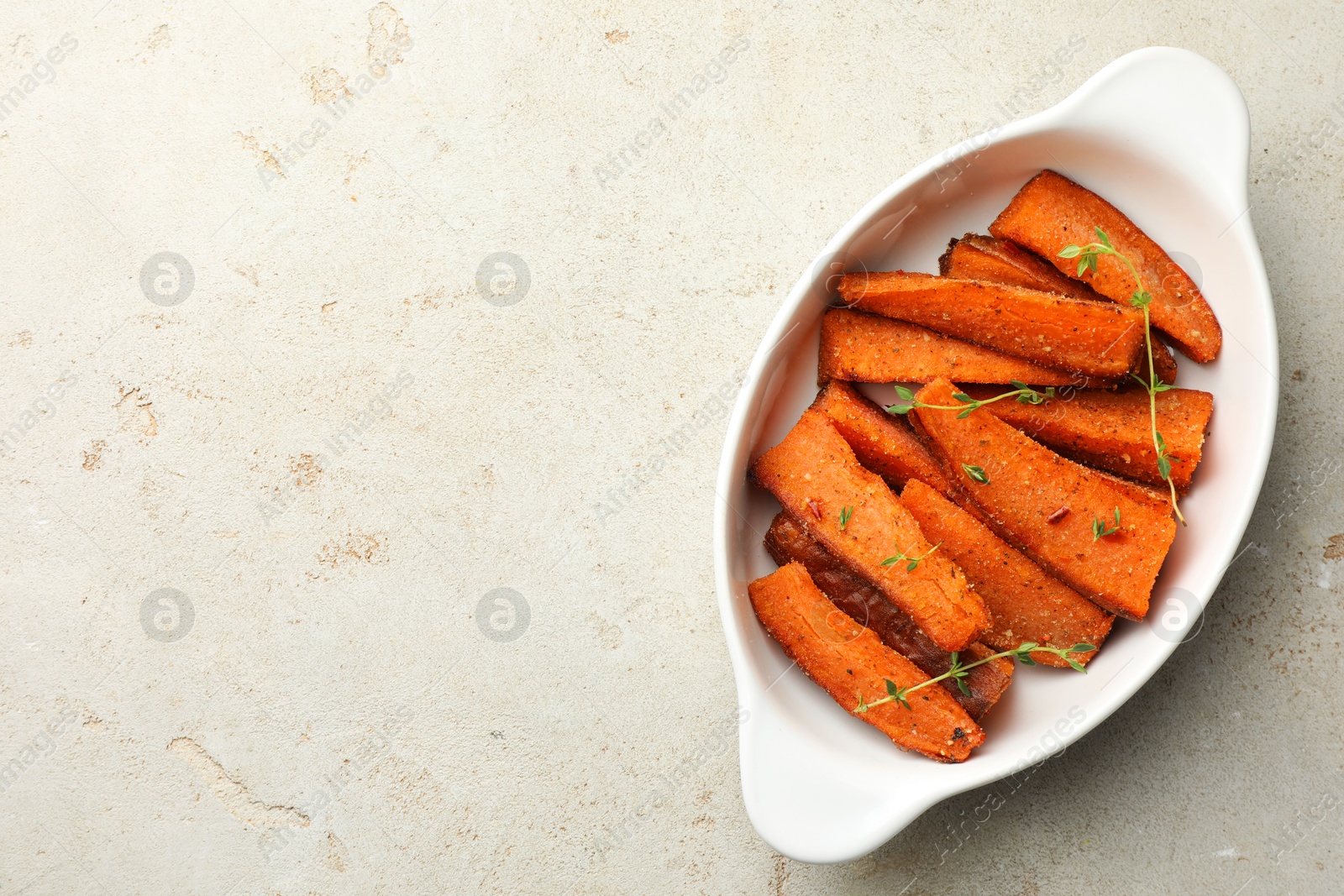 Photo of Pieces of tasty cooked sweet potato with microgreens in baking dish on light textured table, top view. Space for text