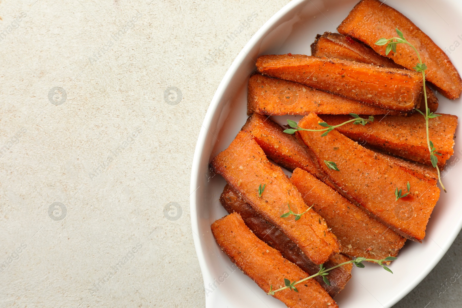 Photo of Pieces of tasty cooked sweet potato with microgreens in baking dish on light textured table, top view. Space for text