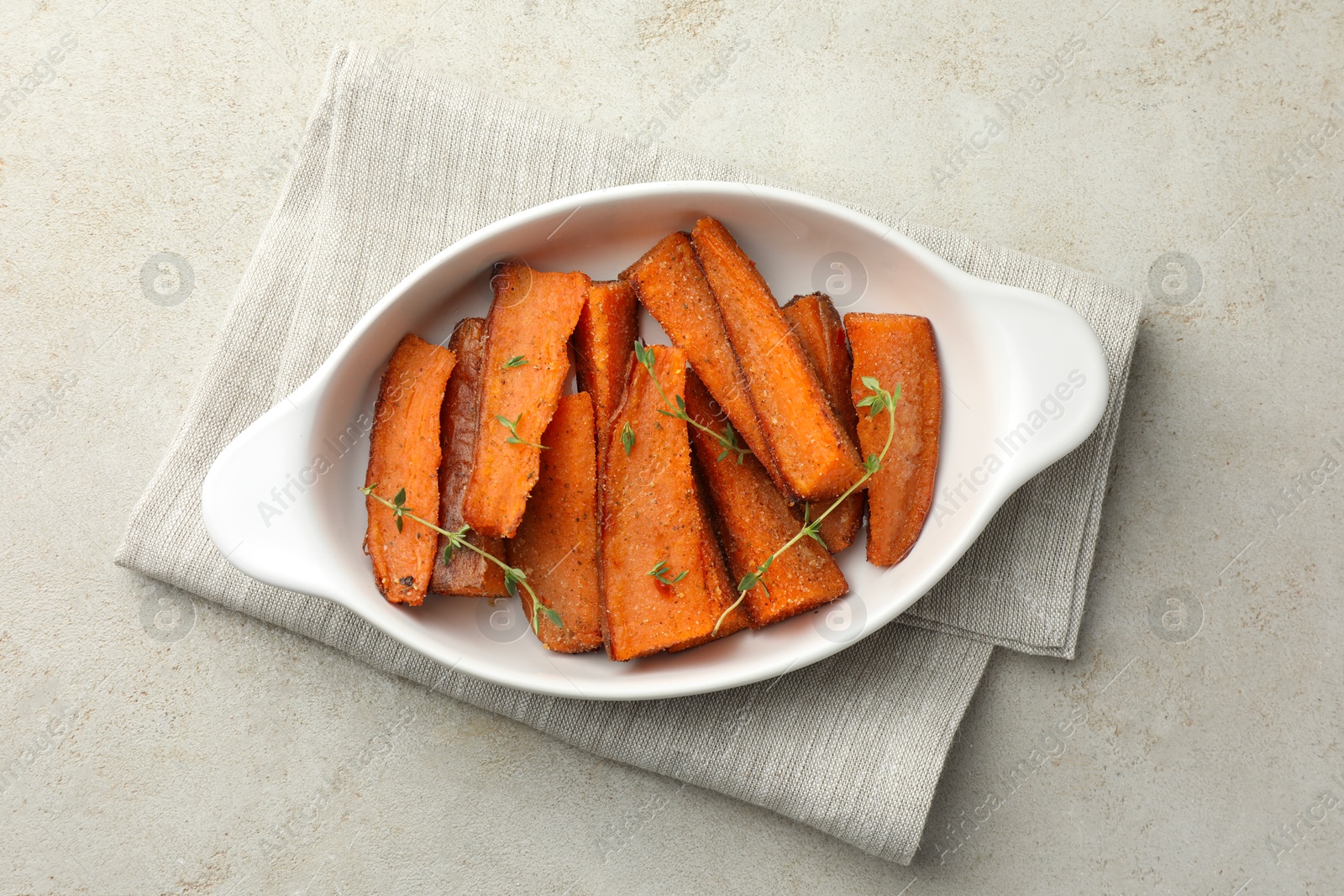 Photo of Pieces of tasty cooked sweet potato with microgreens in baking dish on light textured table, top view