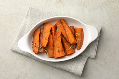 Photo of Pieces of tasty cooked sweet potato with microgreens in baking dish on light textured table, top view