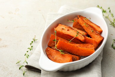 Photo of Pieces of tasty cooked sweet potato in baking dish with microgreens on light textured table