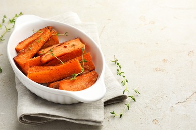 Photo of Pieces of tasty cooked sweet potato in baking dish with microgreens on light textured table. Space for text