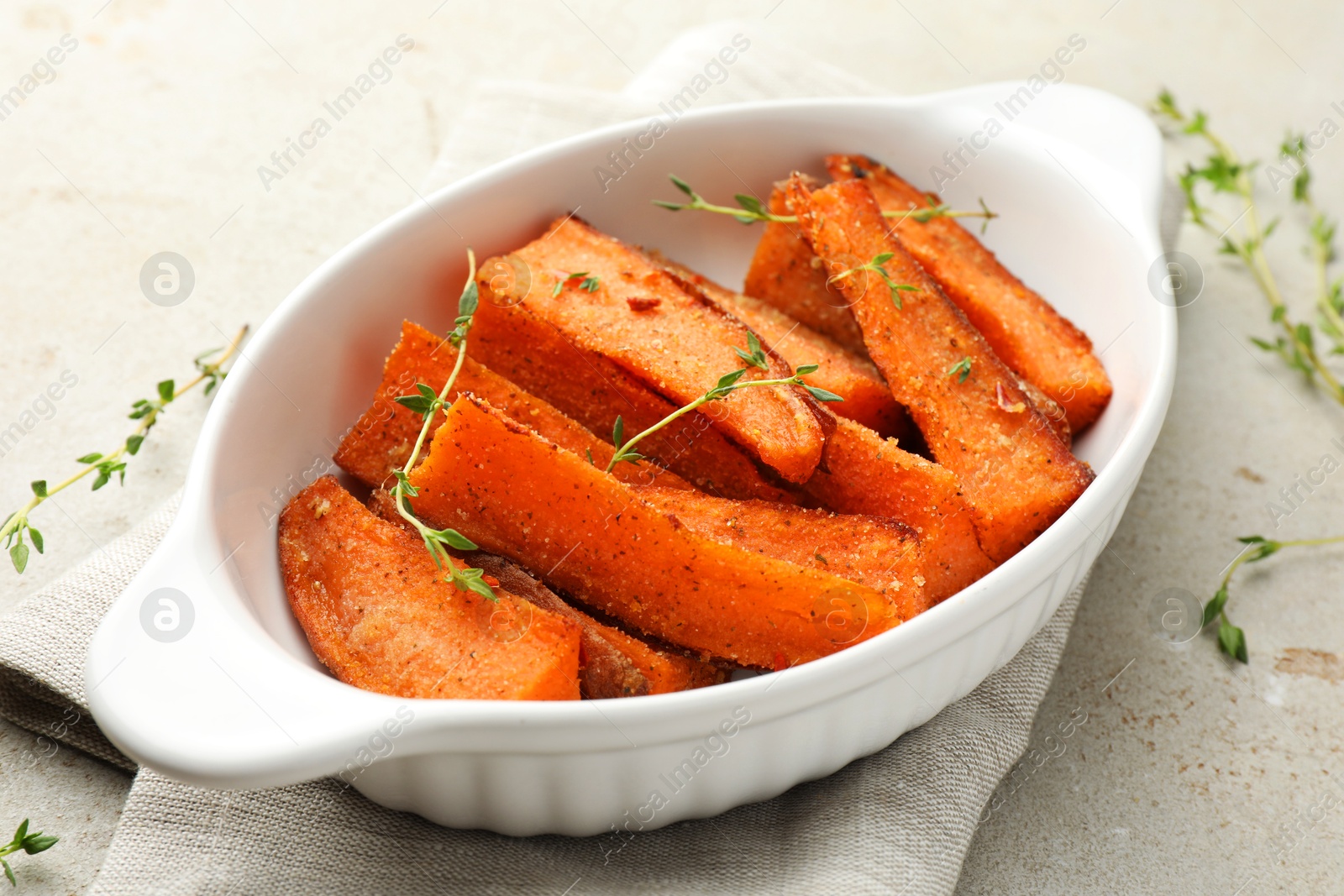 Photo of Pieces of tasty cooked sweet potato in baking dish with microgreens on light textured table, closeup