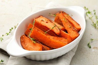 Photo of Pieces of tasty cooked sweet potato in baking dish with microgreens on light textured table, closeup