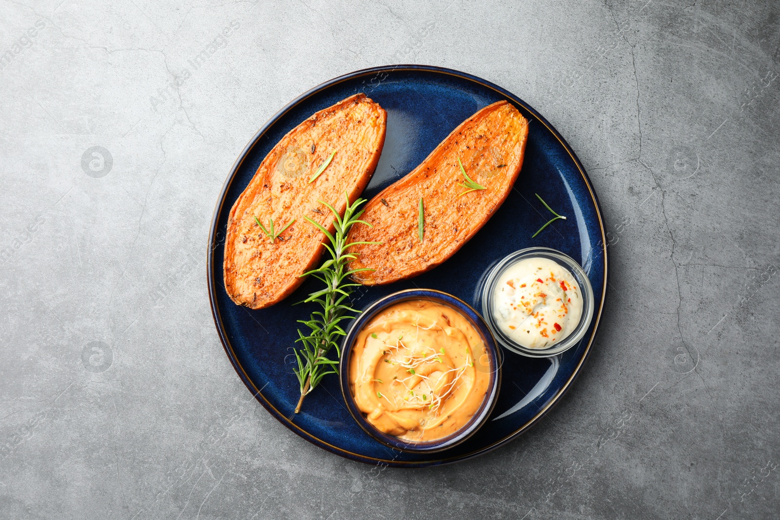 Photo of Halves of tasty baked sweet potato served with sauces on grey textured table, top view