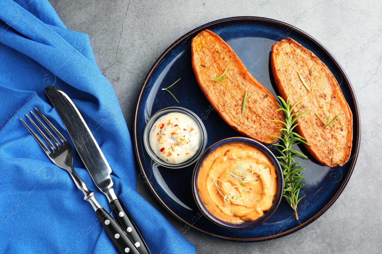 Photo of Halves of tasty baked sweet potato served on grey textured table, flat lay