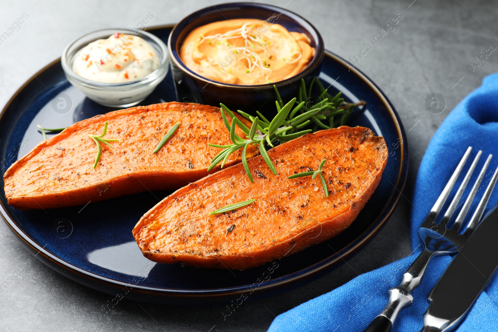 Photo of Halves of tasty baked sweet potato served on grey textured table